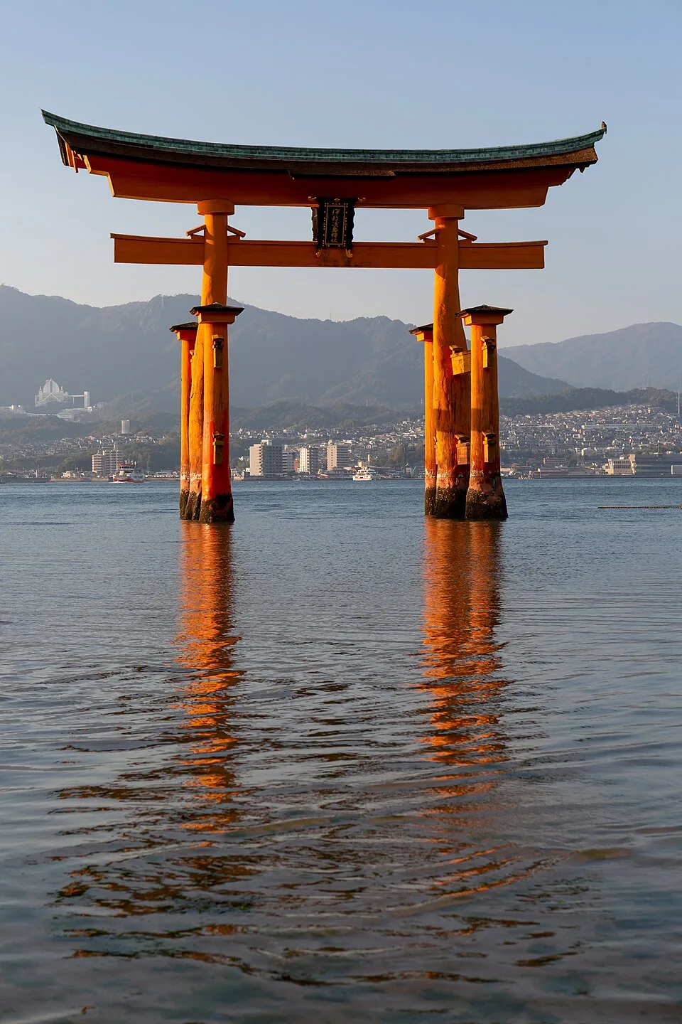 The large vermilion torii of Itsukushima Shrine standing in shallow water with mountains behind it