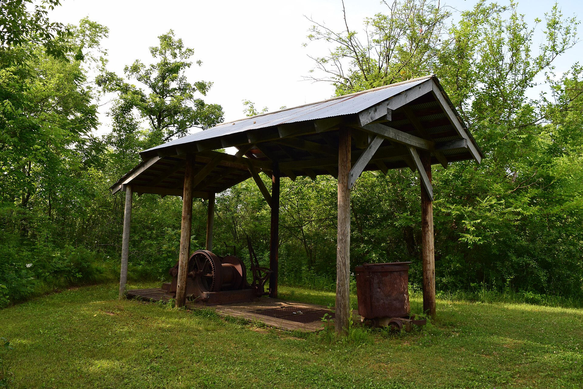 Historic rusted mining machinery under an open wooden shelter on green Mineral Point Hill